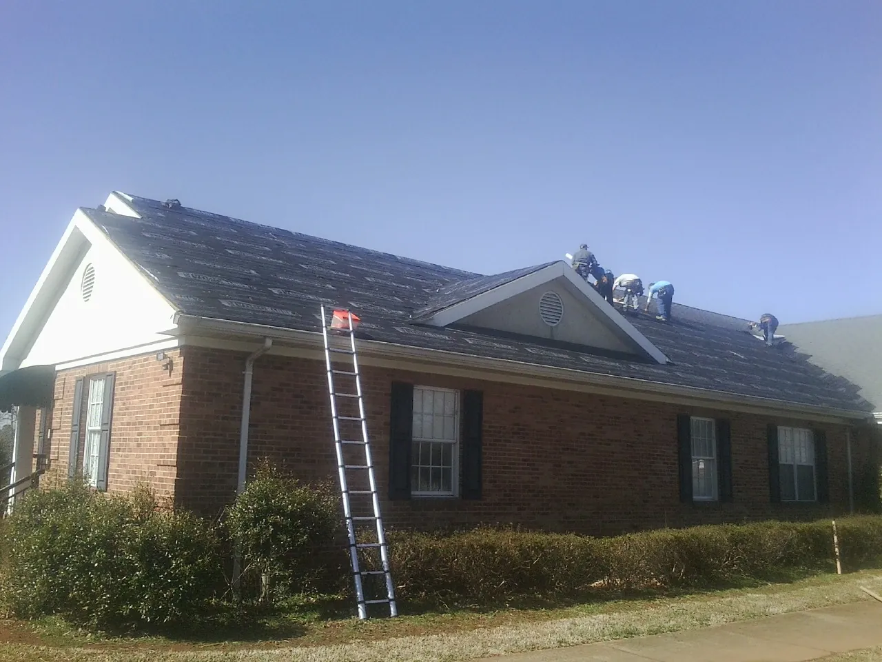Crew tearing shingles off a brick ranch roof with a ladder set — Emergency Roof Repair work by our crew in Maryland Heights