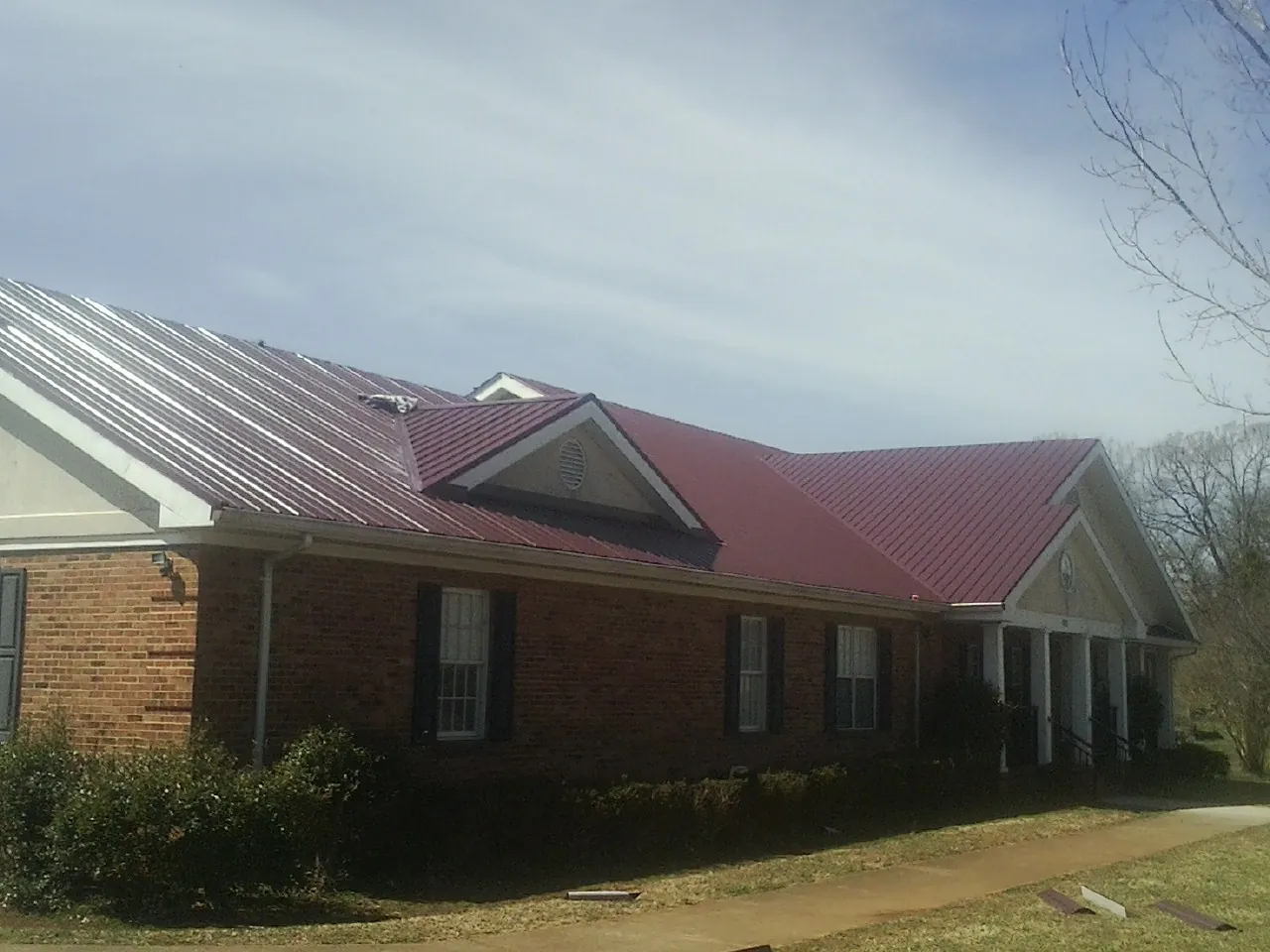 Red metal roof with gabled entries on a long brick building, from a Hail Damage Roof Repair job in Maryland Heights