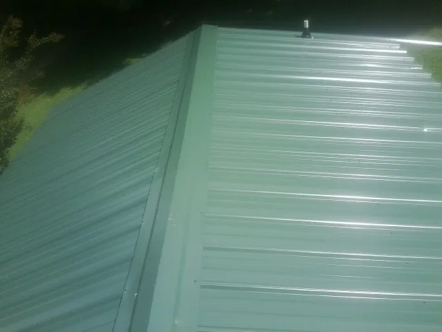 New green metal panels meeting at the ridge of a roof — Flat Roof Repair work by our crew in Maryland Heights