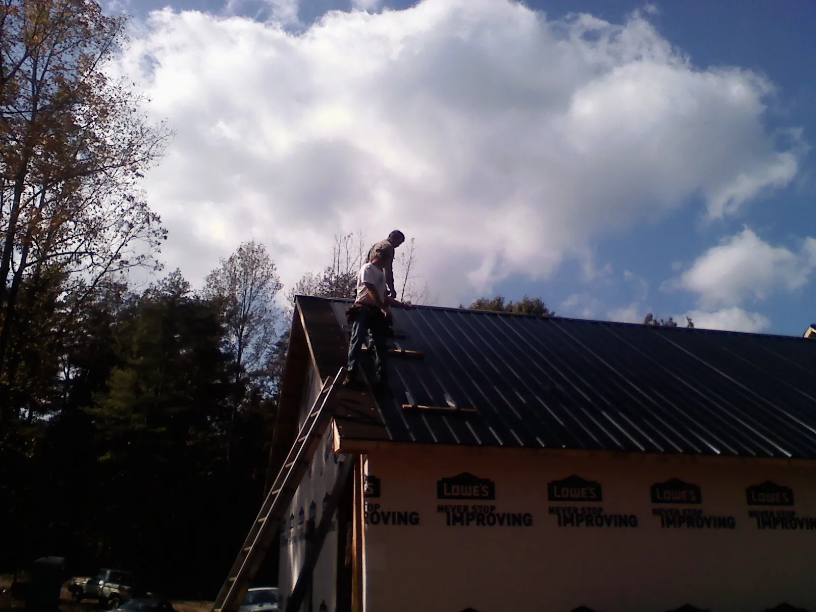 Roofer fastening dark metal panels high against a cloudy sky, from a Roof Inspection job in Maryland Heights