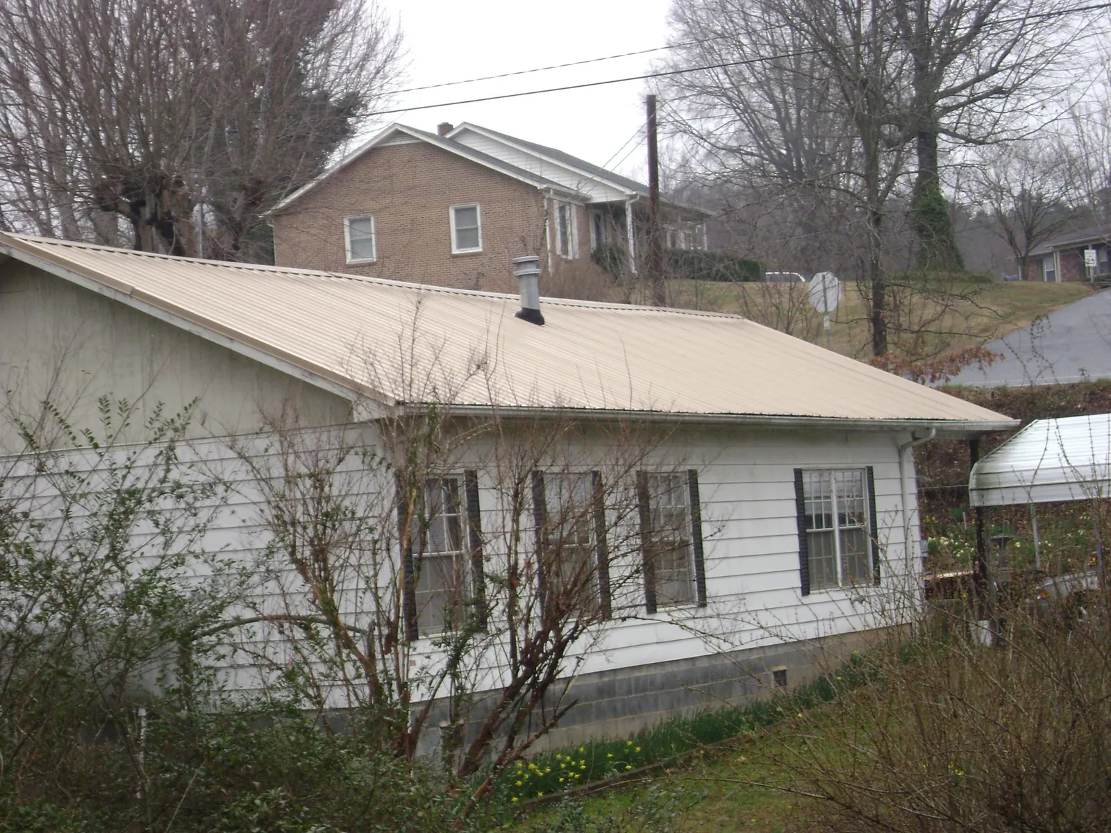 Tan metal roof on a white sided house set into a hillside — Commercial Roofing by Roofing Brothers in Maryland Heights